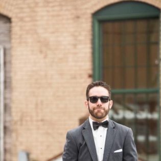 Paul Ledoux in tuxedo, hands in pockets, standing in front of a building